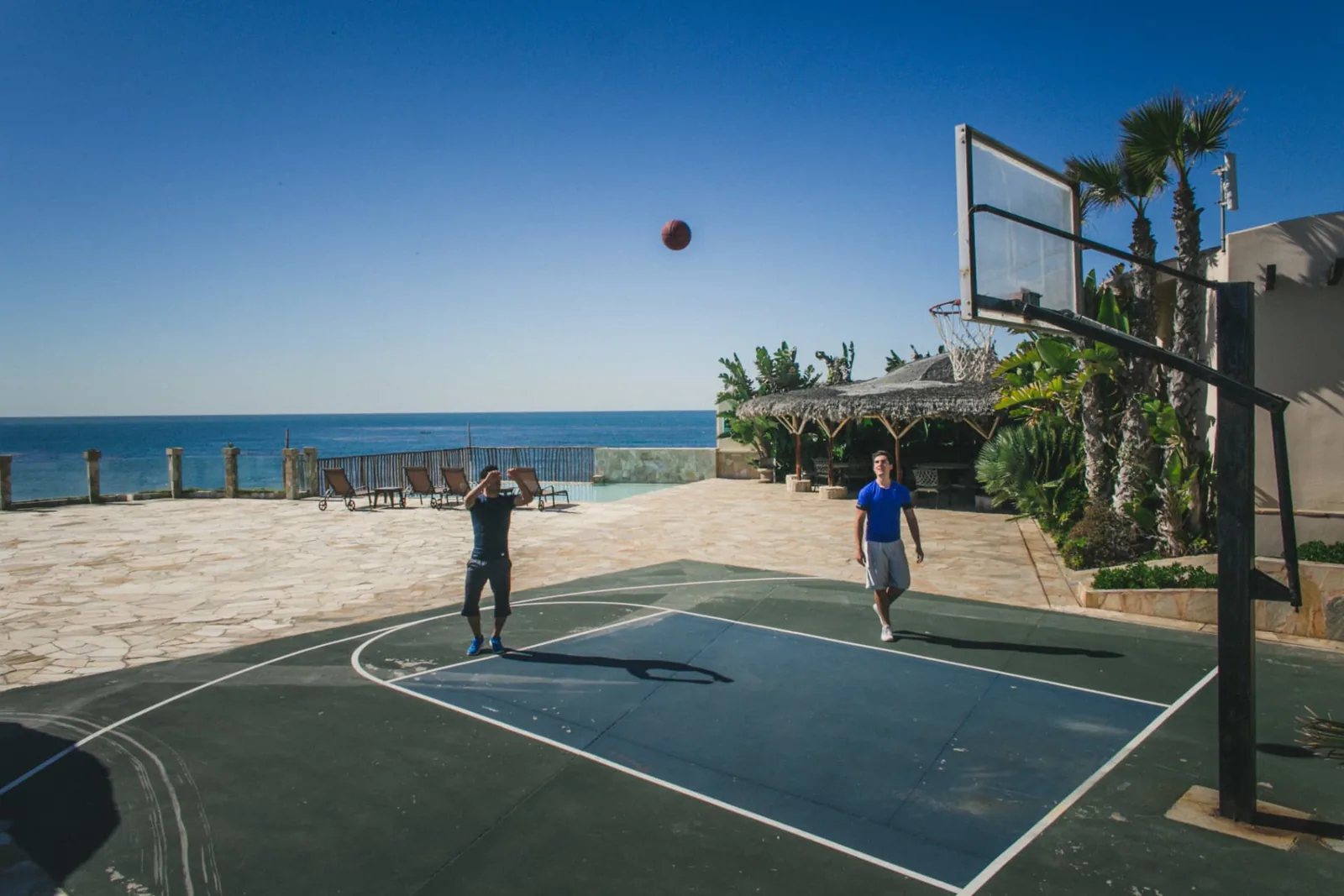Two residents playing basketball on the outdoor court beside the ocean
