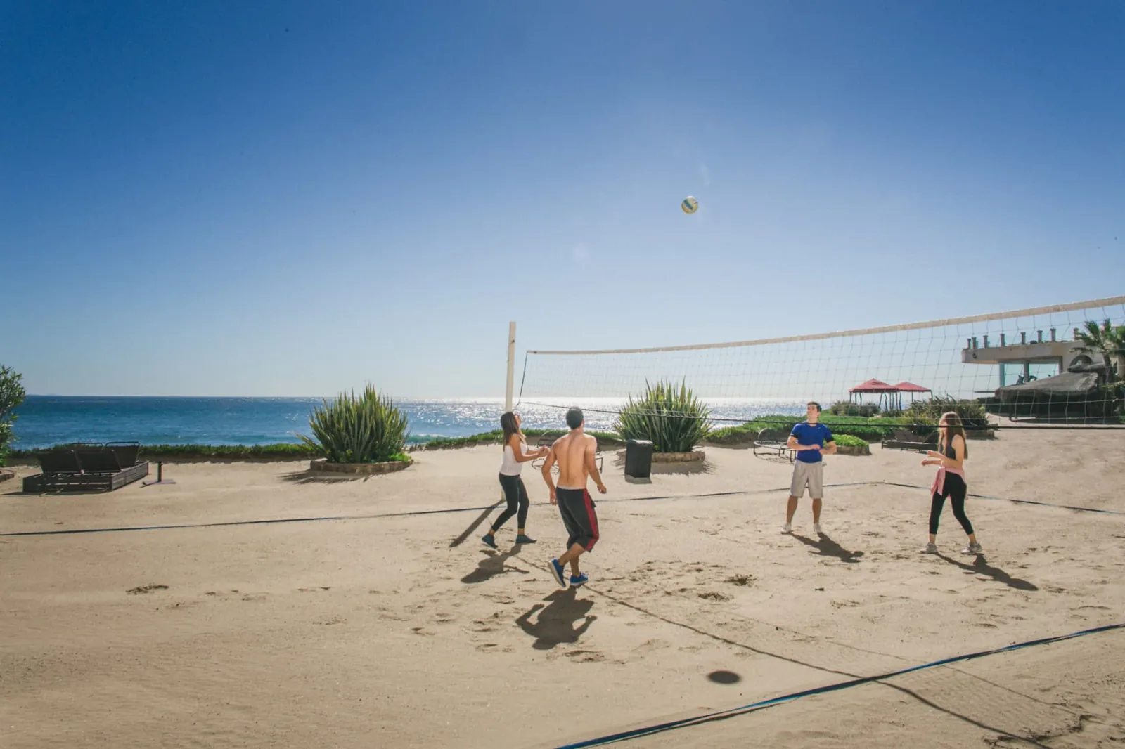 Four residents playing volleyball on the sand court beside the Pacific
