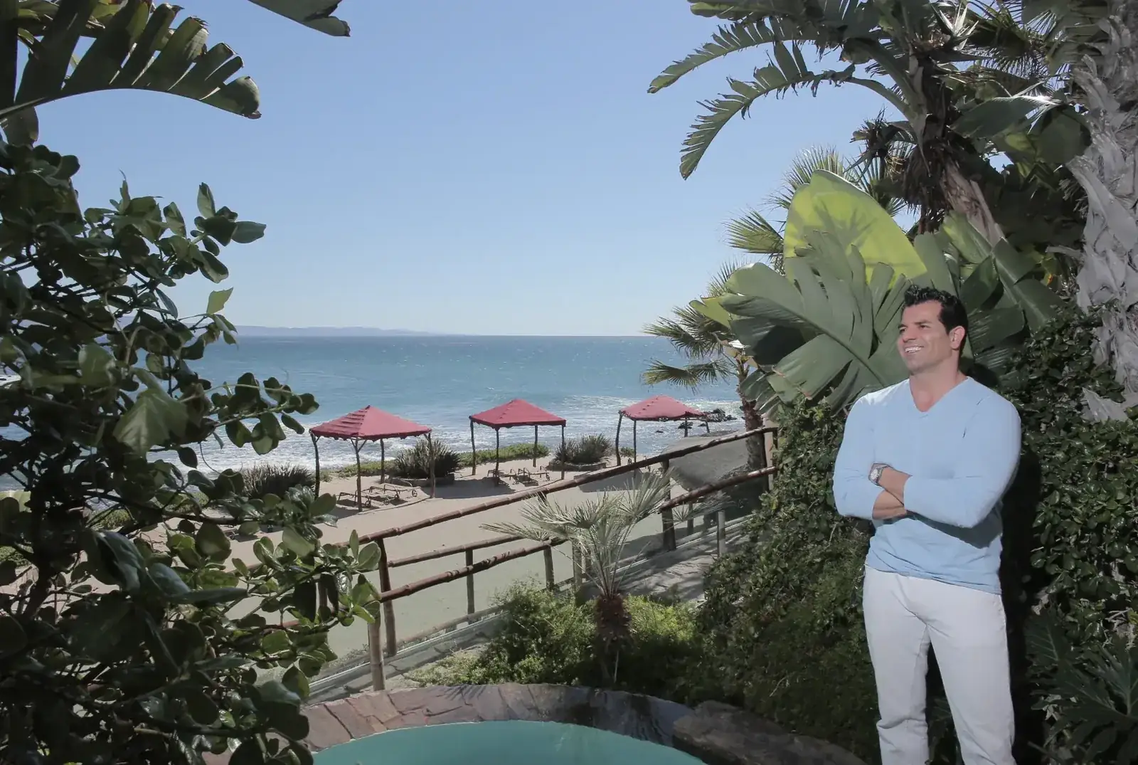 Johnny Tabaie standing among palms on the oceanfront terrace at Holistic Sanctuary