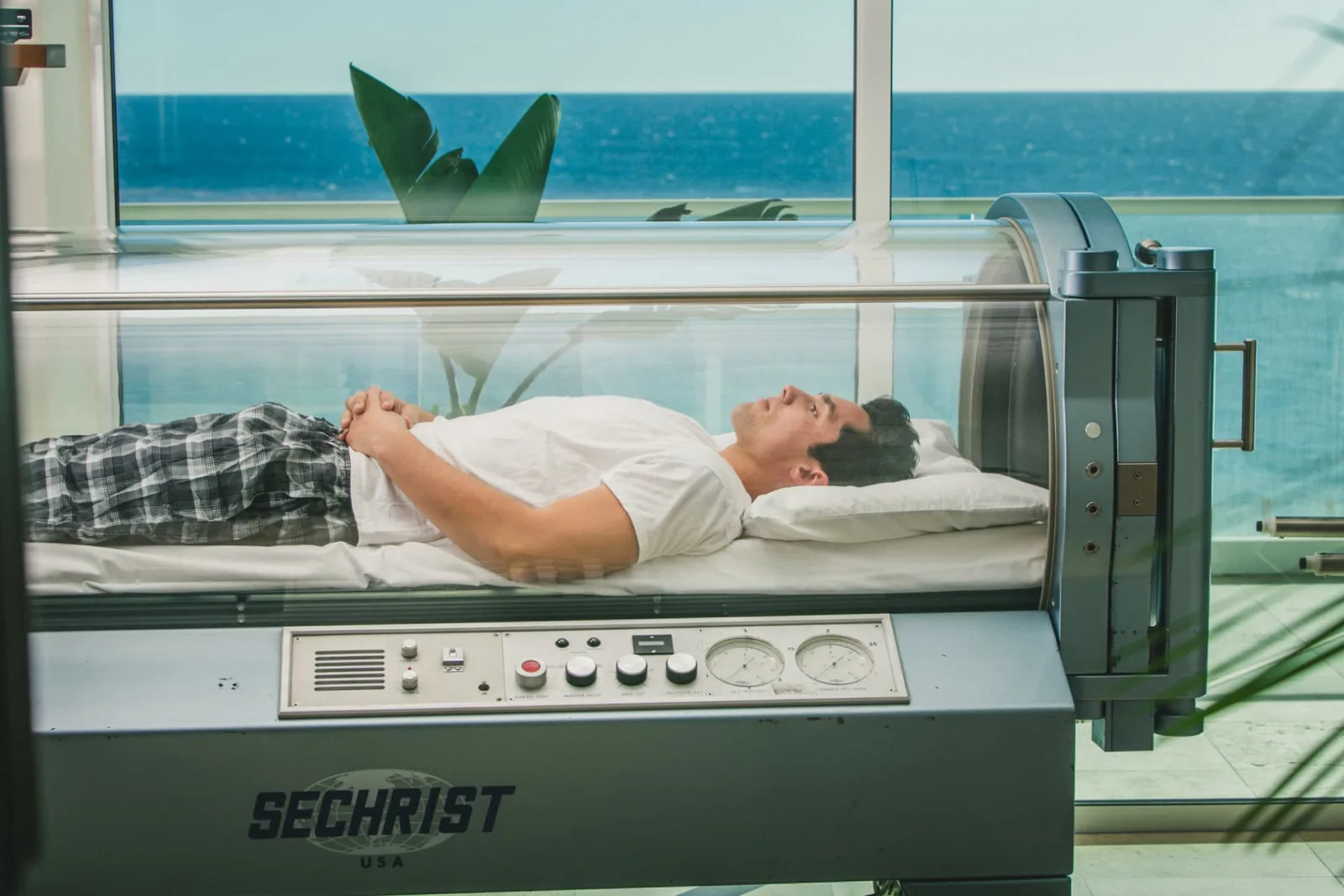 Resident lying inside a Sechrist hyperbaric oxygen chamber beside a window facing the sea