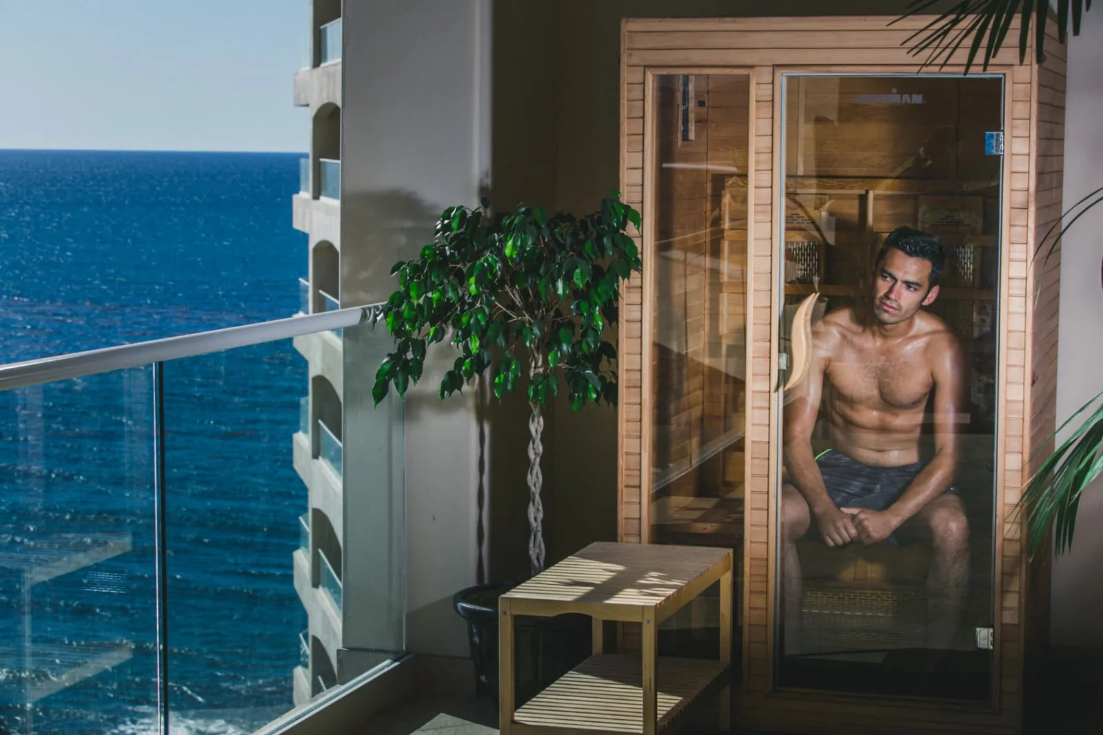 Resident sitting inside an infrared sauna cabin beside an ocean-facing balcony