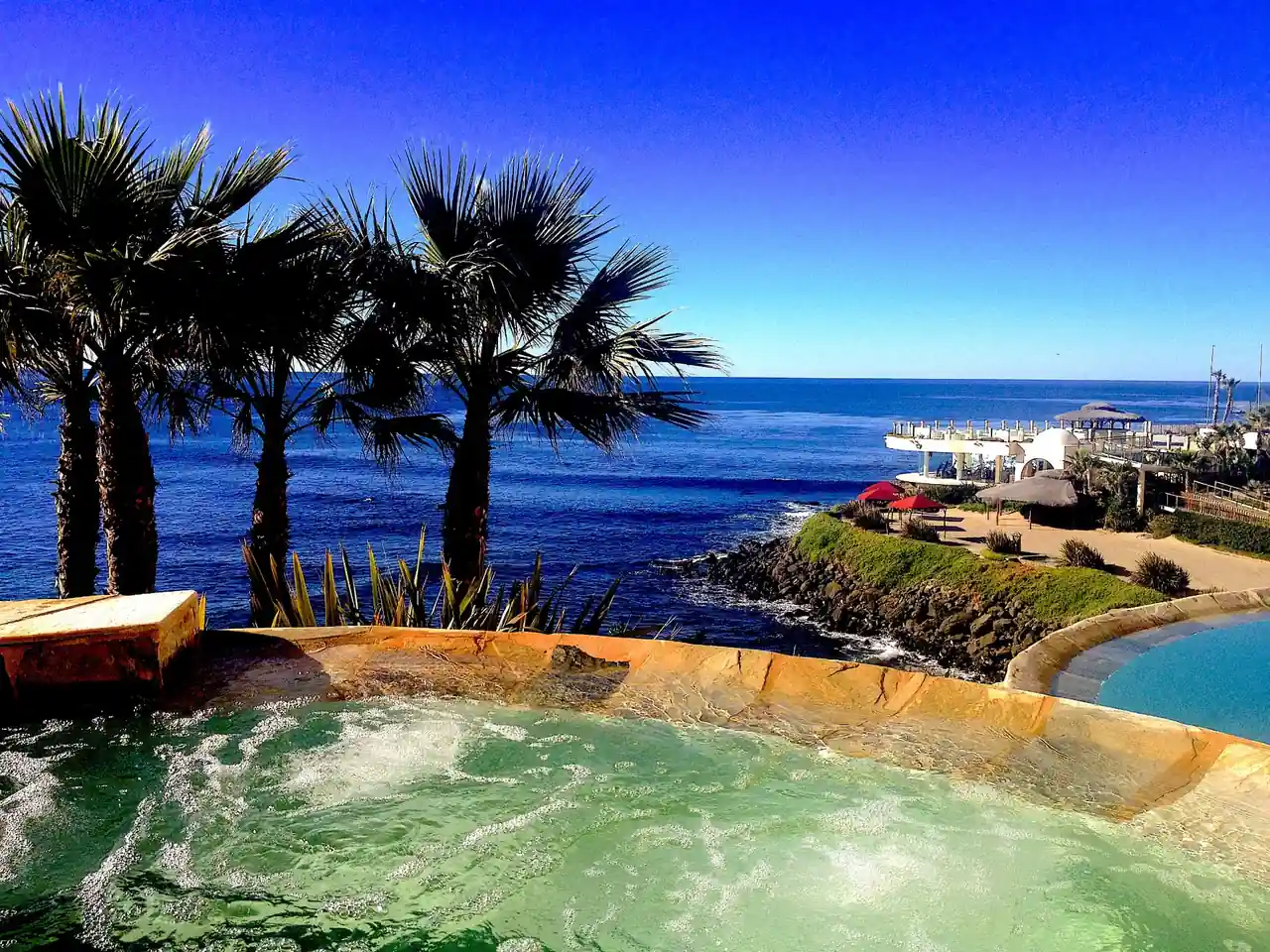 Bubbling jacuzzi framed by palms with the Pacific and the sanctuary terraces beyond