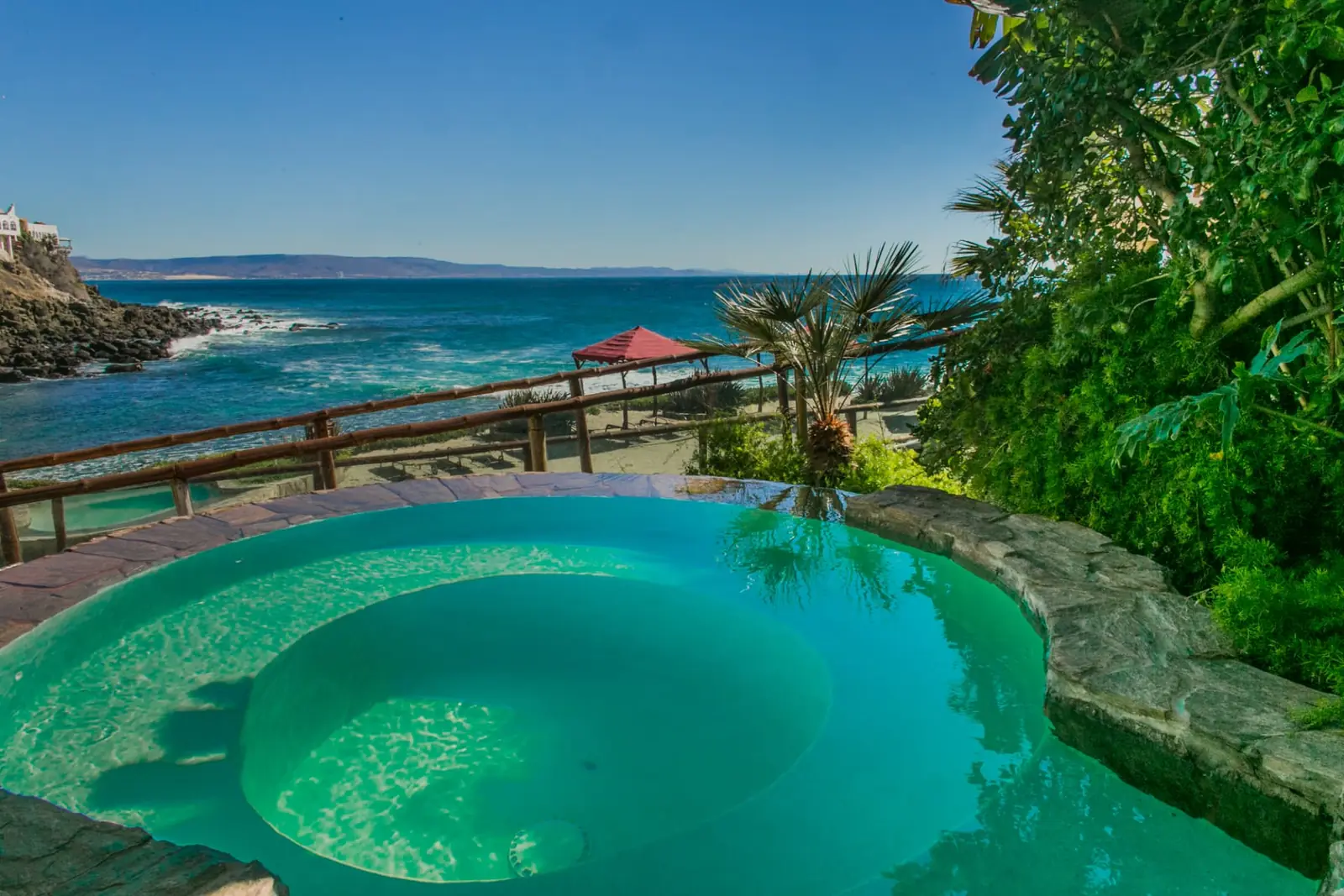 Stone jacuzzi on a garden terrace with the ocean and beach shelters behind