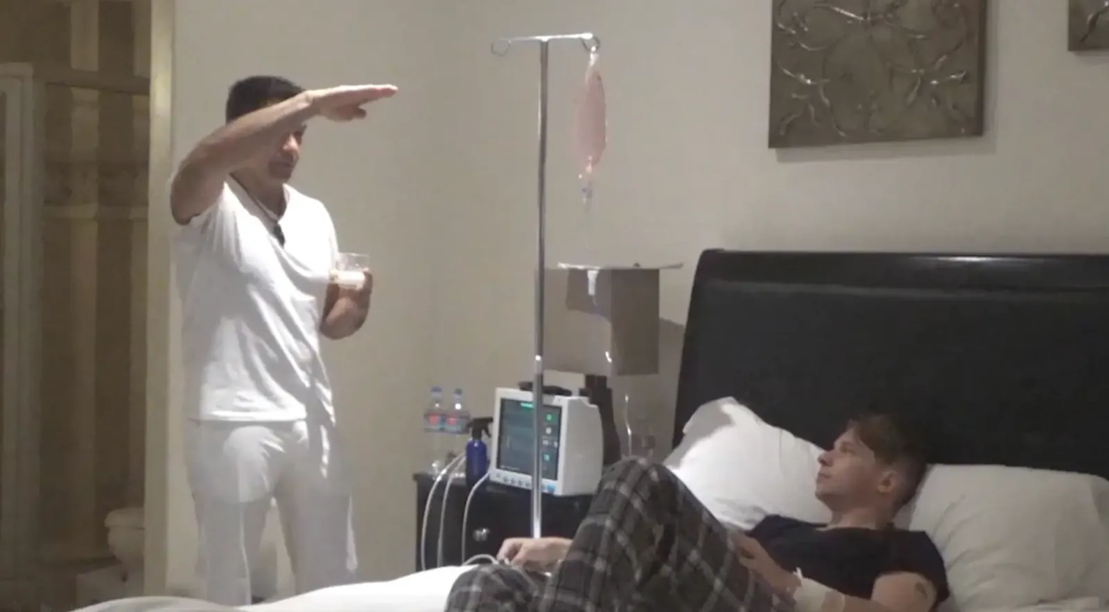 Johnny Tabaie explaining what to expect to a resident resting in bed beside an IV line and vital-signs monitor