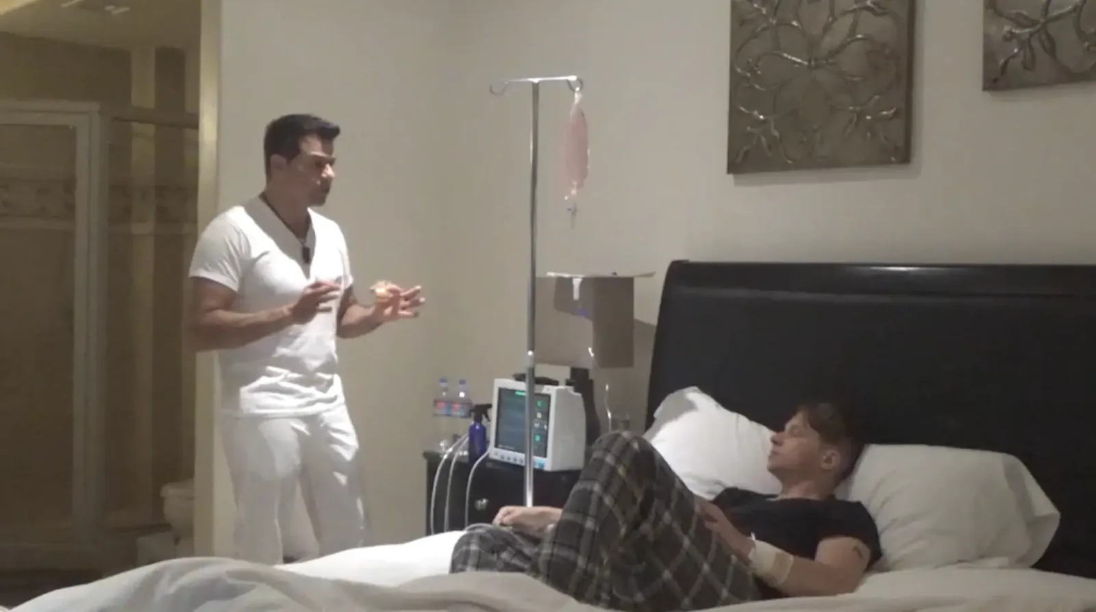 Johnny Tabaie speaking with a resident who is resting in bed with an IV line and a vital-signs monitor