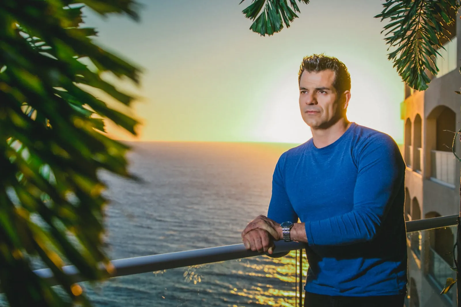 Johnny Tabaie, founder of Holistic Sanctuary, on a balcony overlooking the ocean at sunset