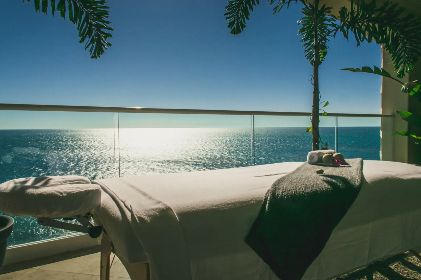 Prepared massage table on a palm-framed balcony above the ocean at Holistic Sanctuary