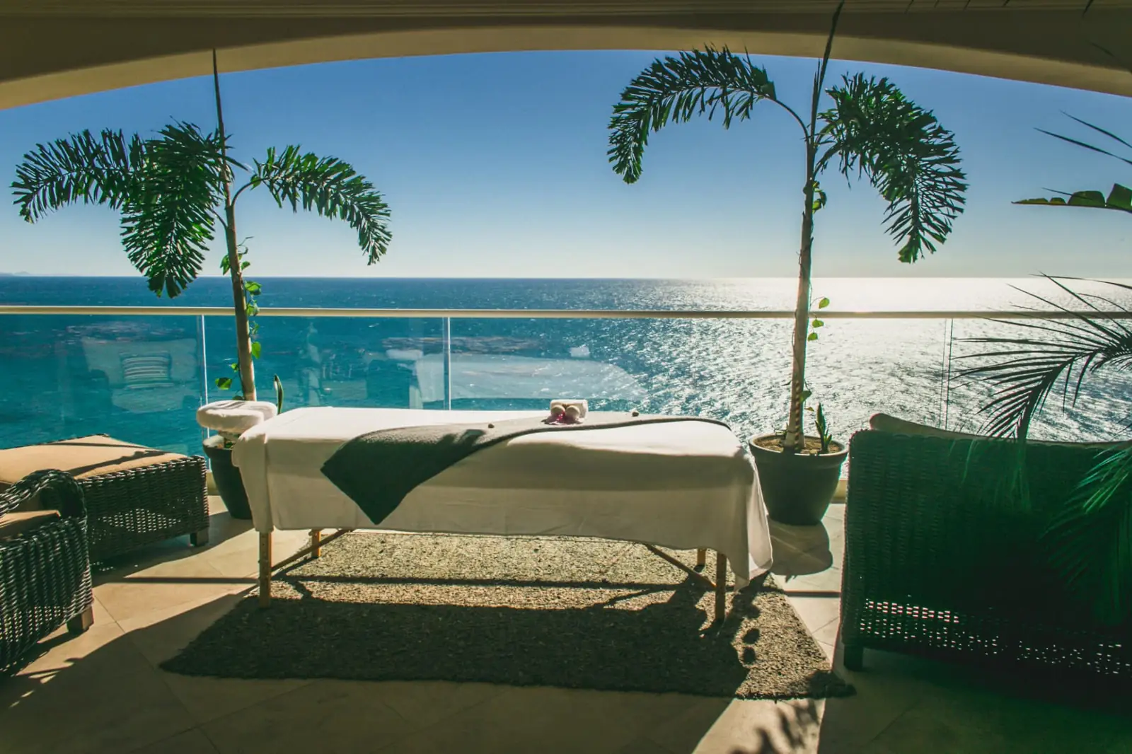 Massage table set up on a shaded oceanfront terrace surrounded by palms