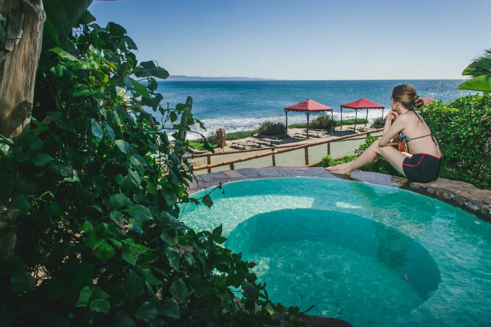 Guest sitting at the edge of a garden pool overlooking the beach and ocean