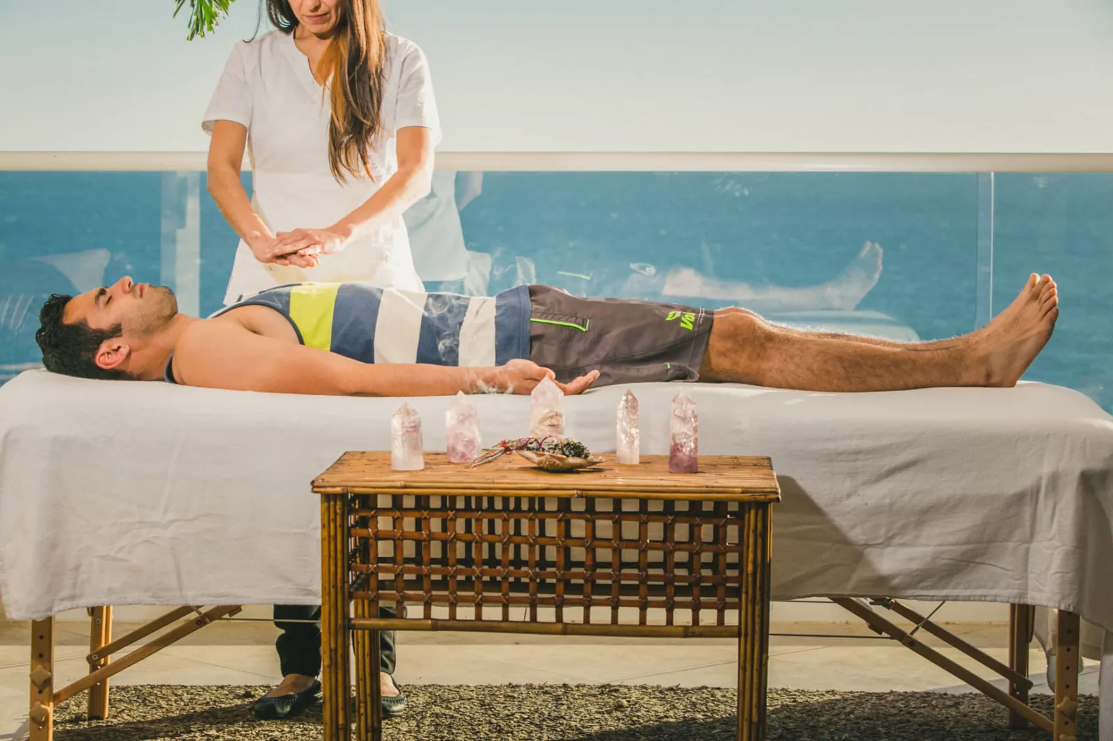 Practitioner holding her hands above a resident lying on a treatment table by the ocean