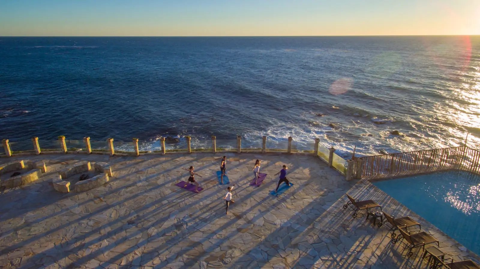 Small group practising yoga at sunset on the oceanfront stone terrace at Holistic Sanctuary