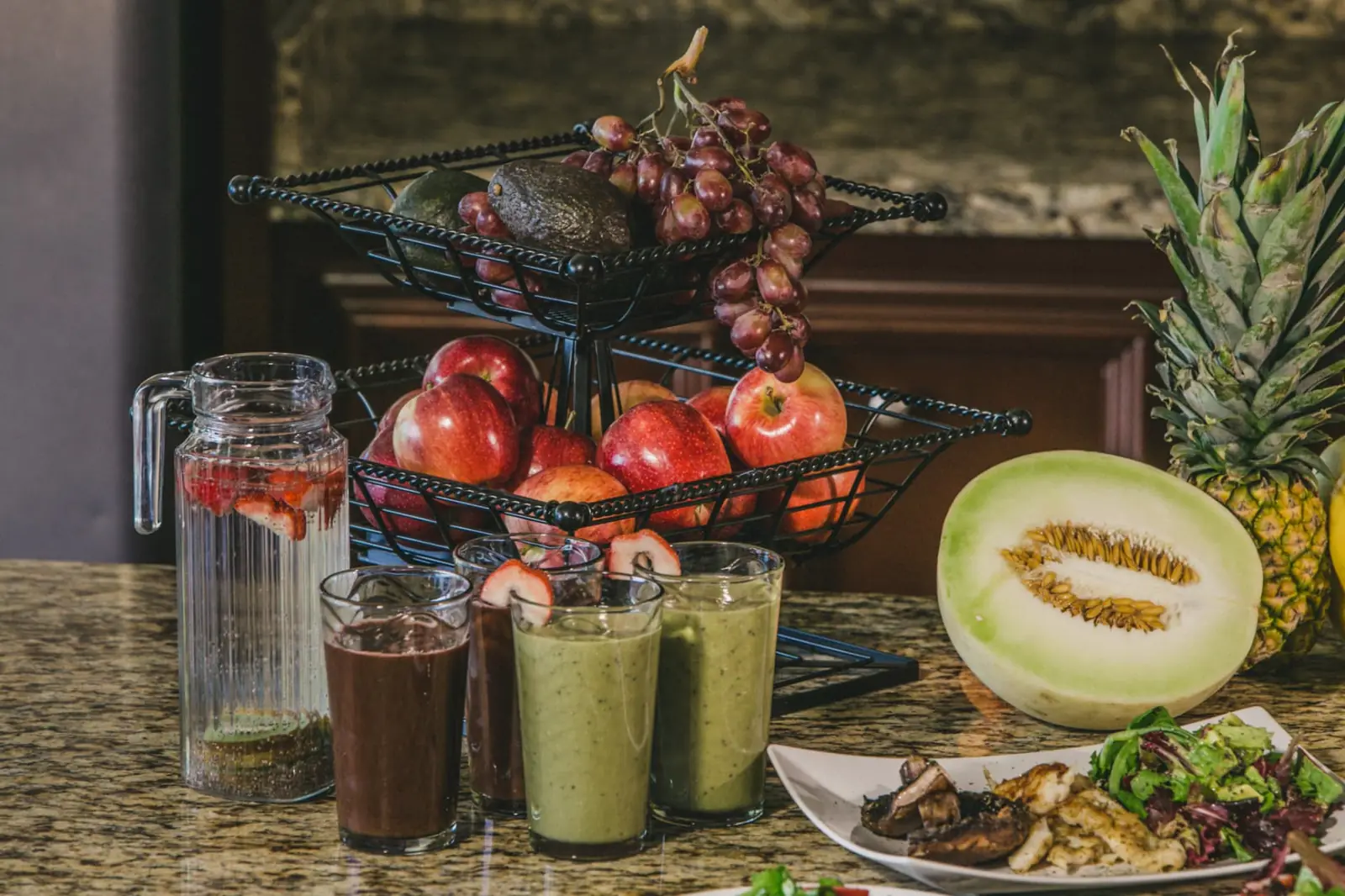 Fresh smoothies, infused water and bowls of organic fruit on a granite counter